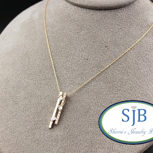 May include: A gold necklace with a vertical pendant featuring multiple small diamonds. The pendant has a geometric design with a mix of shapes. The necklace is displayed on a gray bust. The logo "SJB Sherrie's Jewelry Box" is in the bottom right corner.