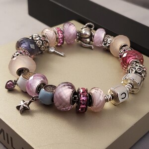 May include: A silver charm bracelet with pink, white, and blue beads. The bracelet features a charm of a teapot, a key, a star, and a letter 'C'.