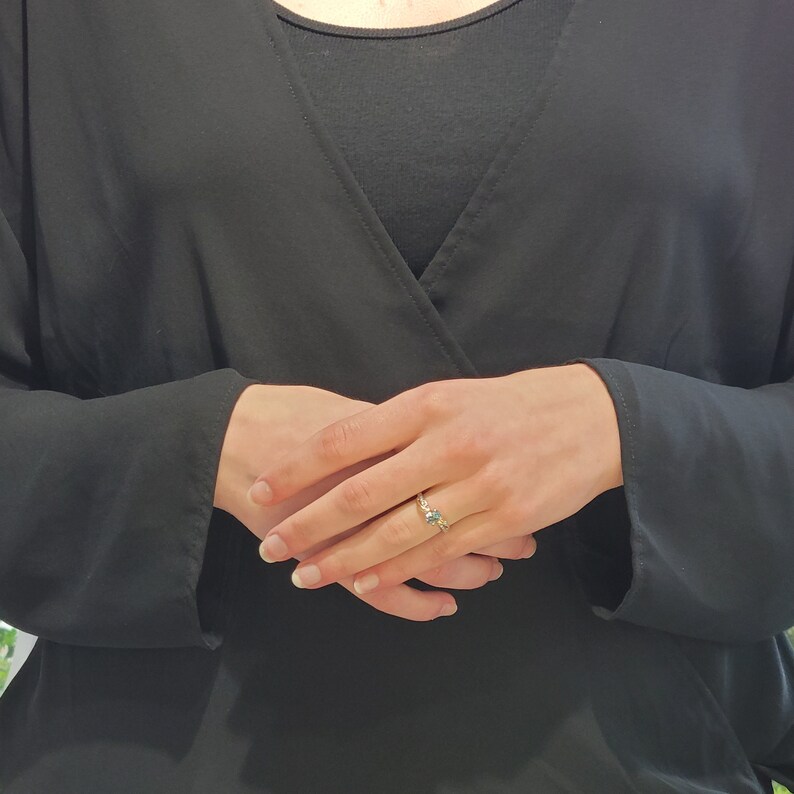 May include: A close-up of a hand wearing a gold ring with a blue gemstone. The ring is on the middle finger of the right hand.