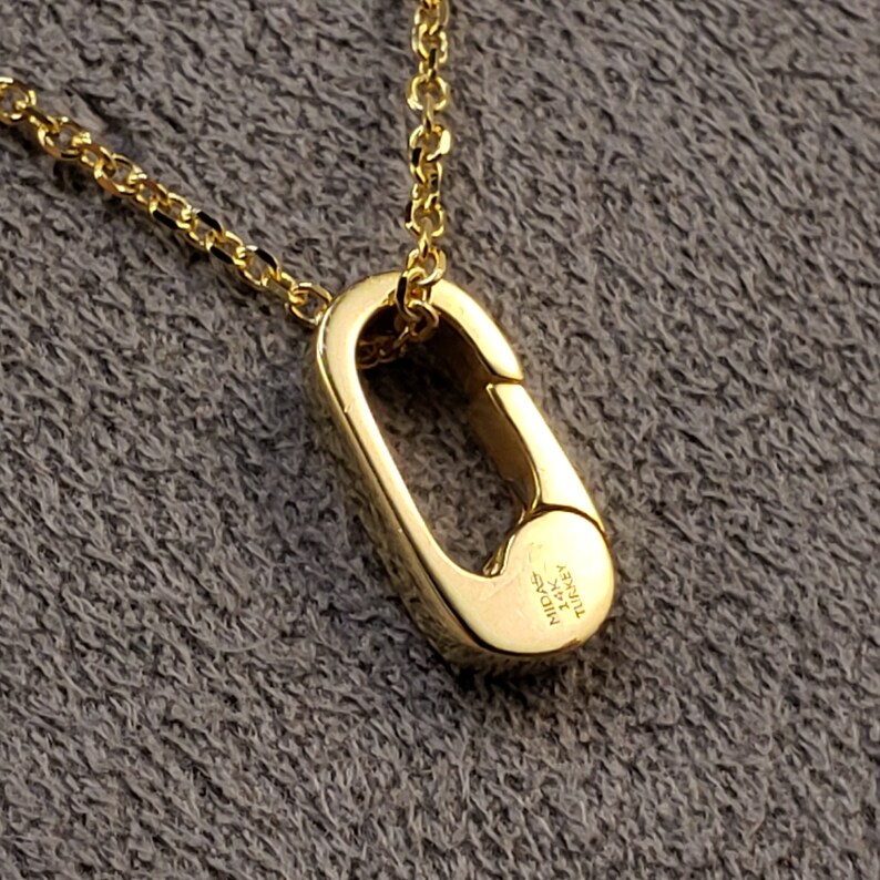May include: A gold chain necklace with a gold clasp pendant. The clasp is oval shaped and has the words "MIDAS" and "TURKEY" engraved on it.