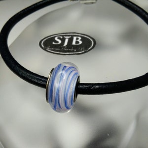 May include: A white glass bead with blue and pink swirls on a black leather bracelet. The bracelet has a silver charm with the text "SJB Jewelry Boutique" on it.