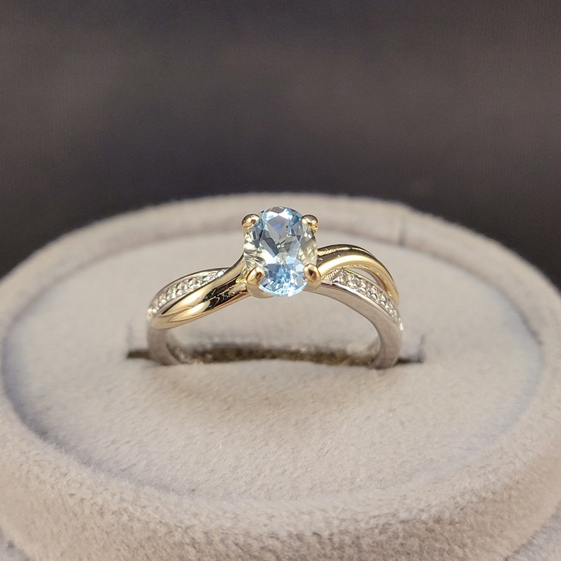 May include: A gold and silver ring with a light blue oval gemstone and smaller clear gemstones set in the band.