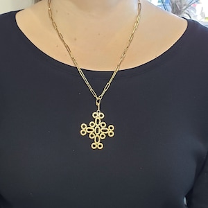 May include: A gold chain necklace with a large, intricate cross pendant. The cross is made of interlocking circles.