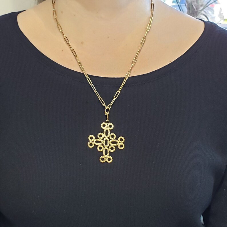 May include: A gold chain necklace with a large, intricate cross pendant. The cross is made of interlocking circles.