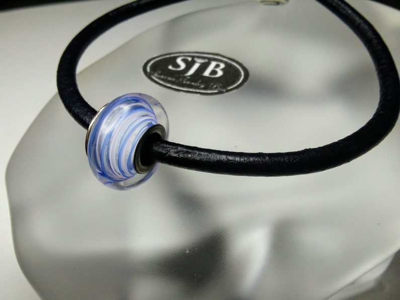 May include: A black leather cord necklace with a white and blue glass bead. The bead has a swirl pattern.