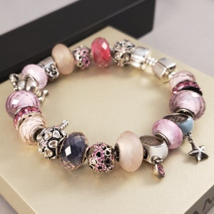 May include: A silver charm bracelet with pink, purple, and blue glass beads, silver charms, and a star charm.