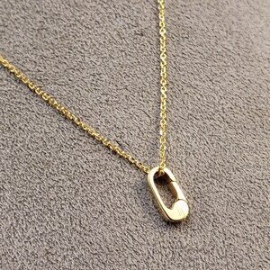 May include: A gold chain necklace with a small, oval-shaped pendant. The pendant has a clasp-like design.