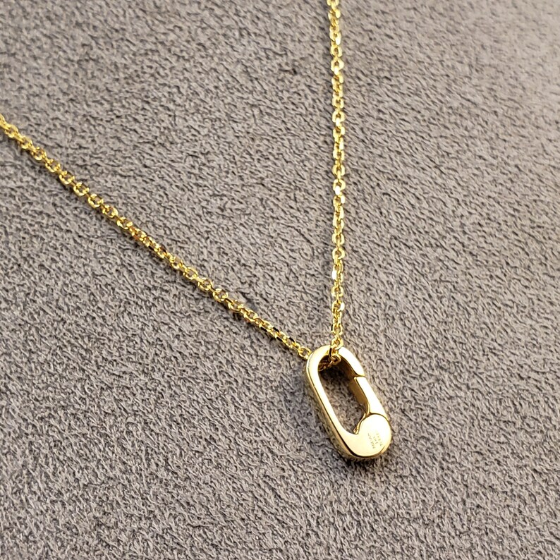 May include: A gold chain necklace with a small, oval-shaped pendant. The pendant has a clasp-like design.