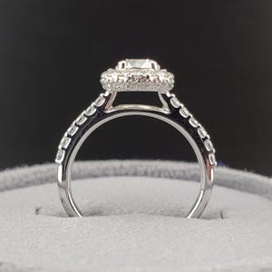 May include: A silver engagement ring with a round center stone surrounded by a halo of smaller stones. The band is also set with smaller stones.