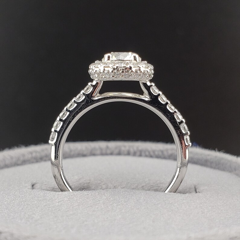May include: A silver engagement ring with a round center stone surrounded by a halo of smaller stones. The band is also set with smaller stones.