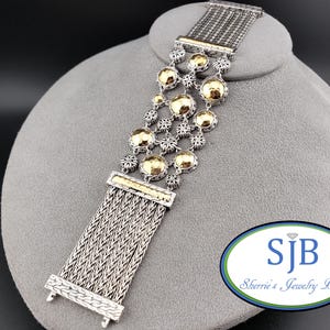 Pode incluir: Pulseira prateada e dourada com um design de corrente entrançada. A pulseira apresenta esferas douradas e detalhes decorativos. A peça é exibida em um busto de joalheria cinza. A pulseira é uma peça marcante.