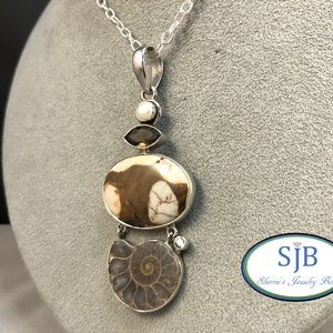 May include: A silver necklace with a pendant featuring a brown and white oval stone, a brown ammonite, a clear gemstone, and a white pearl. The pendant is attached to a silver chain.