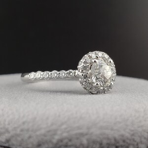 May include: A silver engagement ring with a round center diamond surrounded by a halo of smaller diamonds. The band is also set with small diamonds.