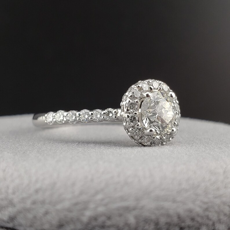 May include: A silver engagement ring with a round center diamond surrounded by a halo of smaller diamonds. The band is also set with small diamonds.