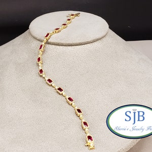 May include: A gold bracelet with red gemstones and small diamonds. The bracelet is on a white display stand. The text "SJB Sherrie's Jewelry Box" is visible in the lower right corner of the image.
