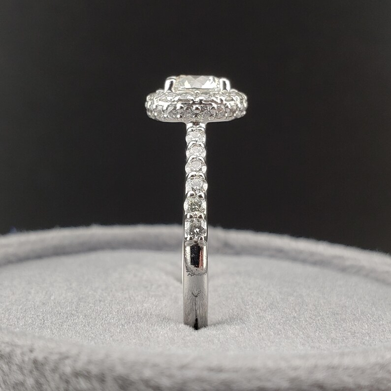May include: A silver ring with a round center stone surrounded by a halo of smaller stones. The band is also set with smaller stones.
