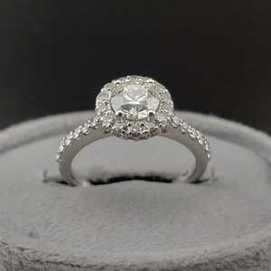 May include: A silver engagement ring with a round center diamond surrounded by a halo of smaller diamonds. The band is also set with smaller diamonds.