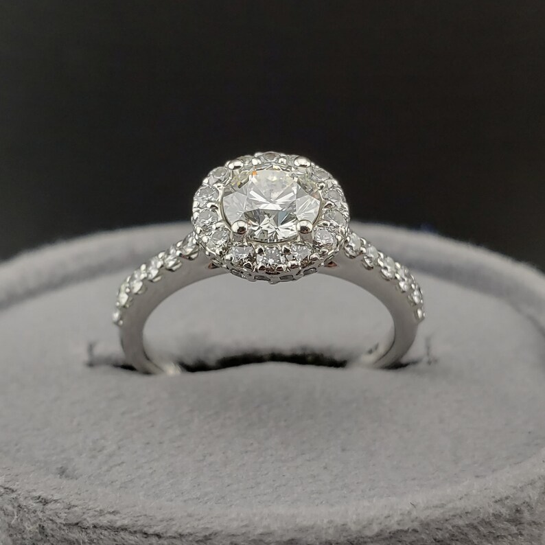 May include: A silver engagement ring with a round center diamond surrounded by a halo of smaller diamonds. The band is also set with smaller diamonds.