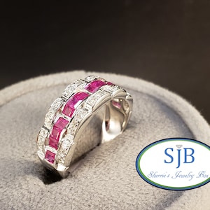 May include: A white gold ring with a band of square-cut pink rubies and diamonds. The ring is set on a gray background with the text "SJB Sherrie's Jewelry Box" visible.