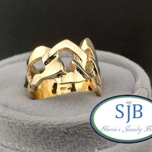 Könnte beinhalten: Ein goldfarbener Ring mit Kettenglied-Design. Der Ring wird auf einer grauen Samtoberfläche präsentiert. Ein auffälliges Schmuckstück.