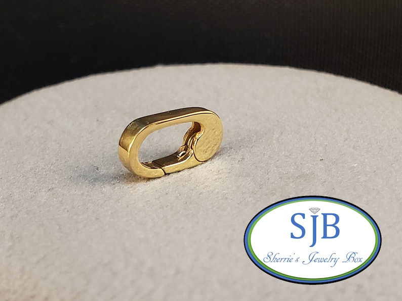 May include: Gold-toned metal clasp with a textured finish. The clasp is oval-shaped and has a spring-loaded mechanism.