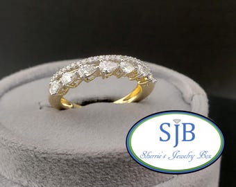 Könnte beinhalten: Ein goldener Ring mit einer Reihe tropfenförmiger Diamanten und kleineren Diamanten. Der Ring liegt auf einer grauen Samtoberfläche. Der Ring stammt von Sherrie's Jewelry Box.