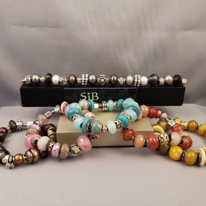 Pu&ograve; includere: Quattro braccialetti colorati con perline e dettagli argentati e dorati. I braccialetti sono impilati uno sopra l'altro. Il braccialetto superiore &egrave; turchese, il successivo &egrave; rosa, il successivo &egrave; rosso e quello inferiore &egrave; giallo.