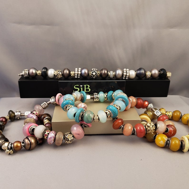 Pu&ograve; includere: Quattro braccialetti colorati con perline e dettagli argentati e dorati. I braccialetti sono impilati uno sopra l'altro. Il braccialetto superiore &egrave; turchese, il successivo &egrave; rosa, il successivo &egrave; rosso e quello inferiore &egrave; giallo.