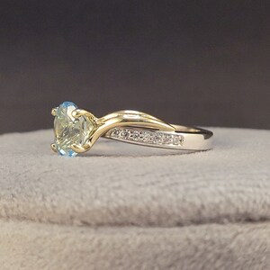 May include: A gold and silver ring with a light blue gemstone and a row of small diamonds.