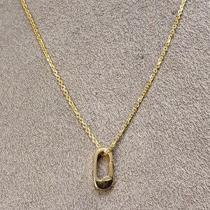 May include: A gold chain necklace with a small, oval-shaped pendant. The pendant is a simple, open design.