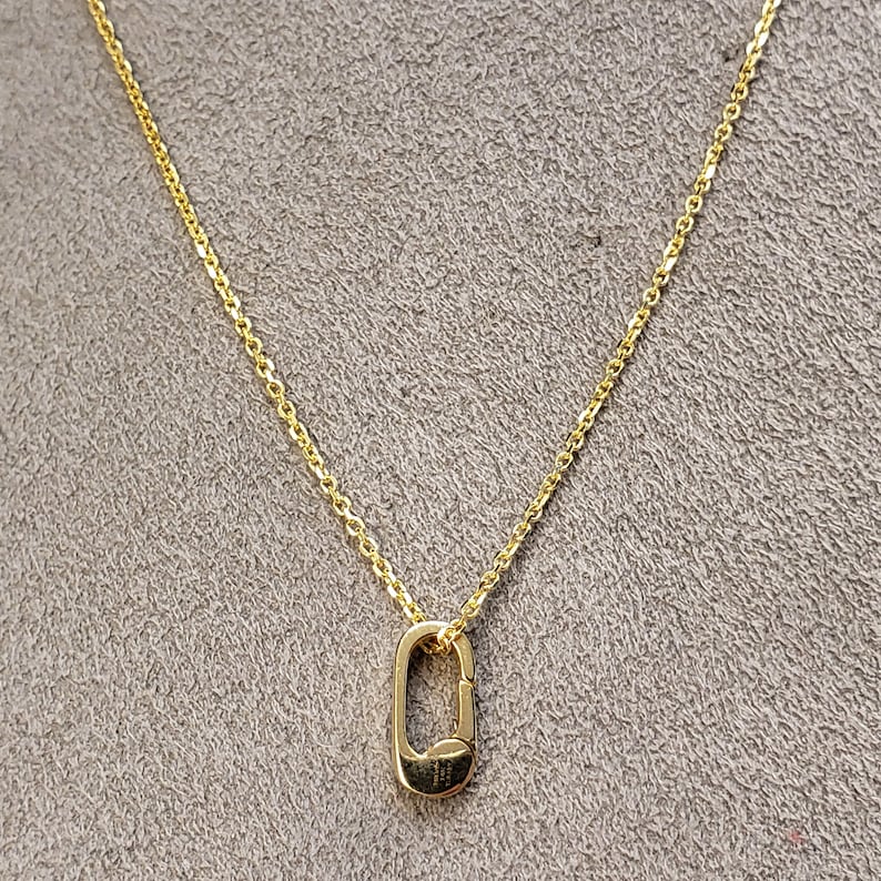 May include: A gold chain necklace with a small, oval-shaped pendant. The pendant is a simple, open design.