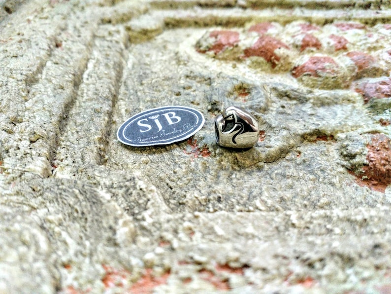 Pu&ograve; includere: Ciondolo in argento con un design a forma di cuore e un adesivo ovale nero con la scritta "SJB - Jewellery Bliss".