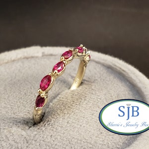 May include: A gold band ring with a row of oval-shaped ruby gemstones. The ring is set in a delicate, curved design.