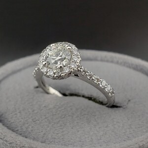 May include: A silver engagement ring with a round center diamond surrounded by a halo of smaller diamonds. The band is also set with smaller diamonds.