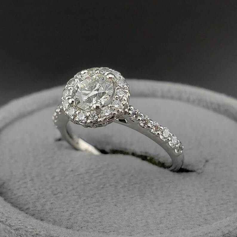 May include: A silver engagement ring with a round center diamond surrounded by a halo of smaller diamonds. The band is also set with smaller diamonds.