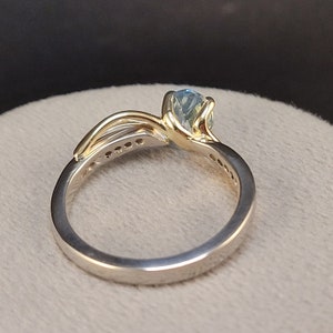 May include: A gold and silver ring with a blue gemstone. The ring has a delicate design with a band of small diamonds.