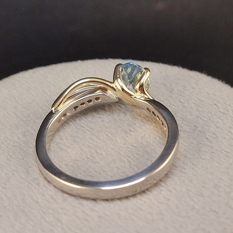 May include: A gold and silver ring with a blue gemstone. The ring has a delicate design with a band of small diamonds.