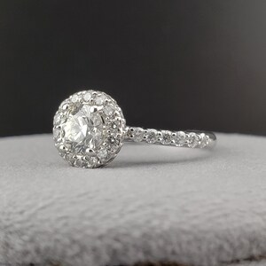 May include: A silver engagement ring with a round center diamond surrounded by a halo of smaller diamonds. The band is also set with smaller diamonds.
