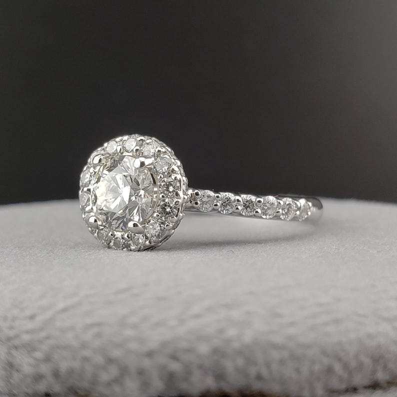 May include: A silver engagement ring with a round center diamond surrounded by a halo of smaller diamonds. The band is also set with smaller diamonds.