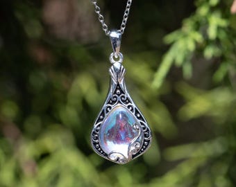 May include: A silver pendant necklace with a teardrop-shaped iridescent glass stone set in an ornate silver frame.
