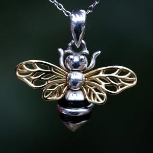 May include: A silver and gold-toned bee pendant necklace. The bee pendant features a detailed design with silver body and head, gold-toned wings, and a black and silver striped abdomen. The necklace has a delicate silver chain.