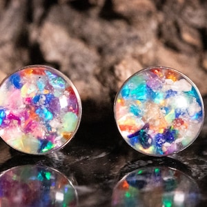 May include: A pair of silver stud earrings with iridescent, multi-colored resin insets. The resin contains small, colorful pieces of glitter and iridescent flakes.