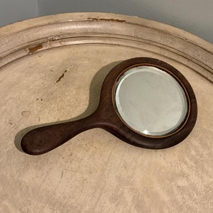 May include: A wooden hand mirror with a dark brown handle and a round, silver-framed mirror.