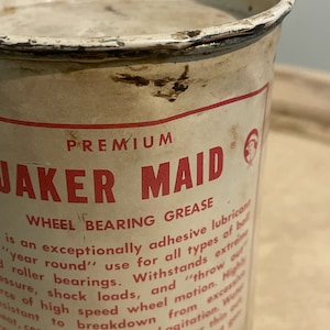 May include: A white metal can with red lettering that reads "PREMIUM JAKER MAID WHEEL BEARING GREASE". The can has a red and white logo with a stylized image of a person. The text on the can describes the product as an "exceptionally adhesive lubricant" for "all types of ball roller bearings".