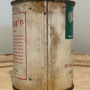 May include: A vintage metal can of Quaker State Super-Test Motor Oil. The can is white with red and green text and a small illustration of a woman. The text on the can reads "Quaker State Super-Test Motor Oil" and "For Farm and Industrial Use".