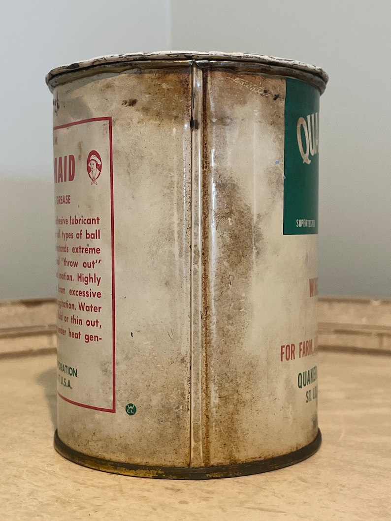 May include: A vintage metal can of Quaker State Super-Test Motor Oil. The can is white with red and green text and a small illustration of a woman. The text on the can reads "Quaker State Super-Test Motor Oil" and "For Farm and Industrial Use".