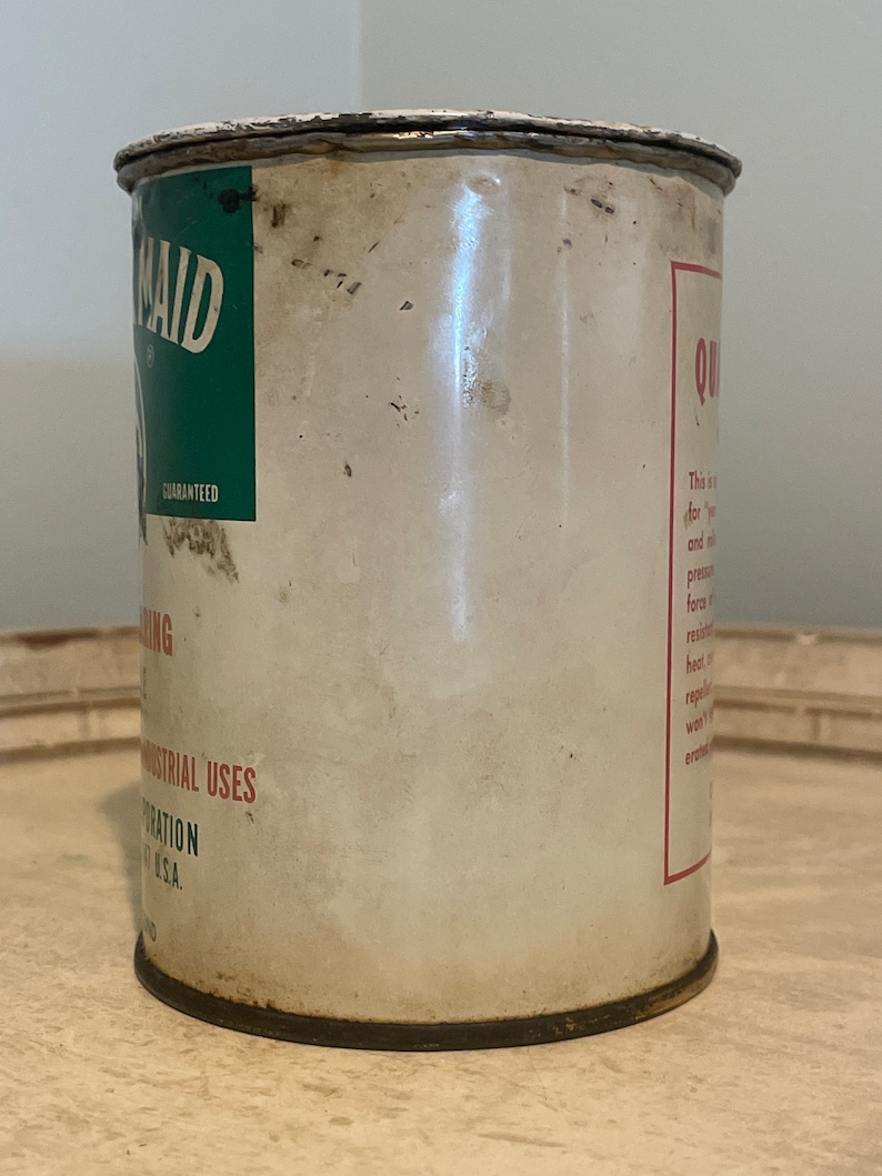 May include: A vintage metal can with a green and white label that says "Maid" and "Guaranteed". The can is labeled "Quik-Drying" and has a red label with text about the product's properties. The can is rusty and has a white background.