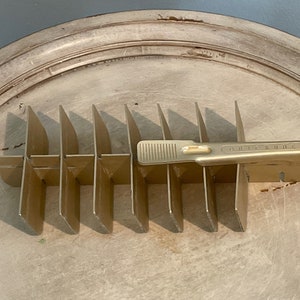 May include: A gold metal coin holder with 10 slots and a lever on the side. The holder is labeled "QUICK KUBE".