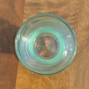 May include: A top-down view of a clear, light green glass vessel with a circular opening. The glass features a thick, rounded rim and a smooth, transparent body that tapers slightly towards the base, showcasing a simple, functional design.