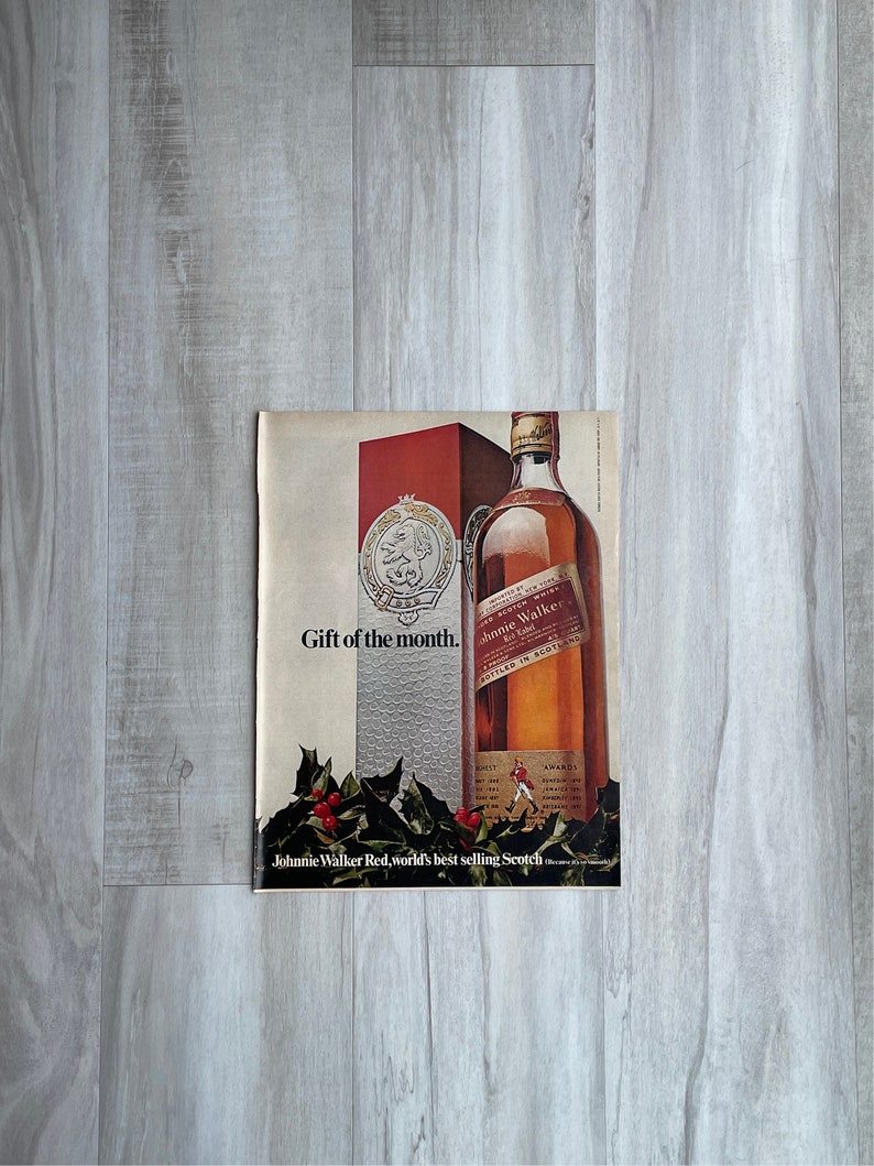 May include: A vintage print advertisement for Johnnie Walker Red Label Scotch whisky. The ad features a bottle of Johnnie Walker Red Label Scotch whisky with a red and gold label. The ad also features the text "Gift of the month." and "Johnnie Walker Red, world's best selling Scotch."